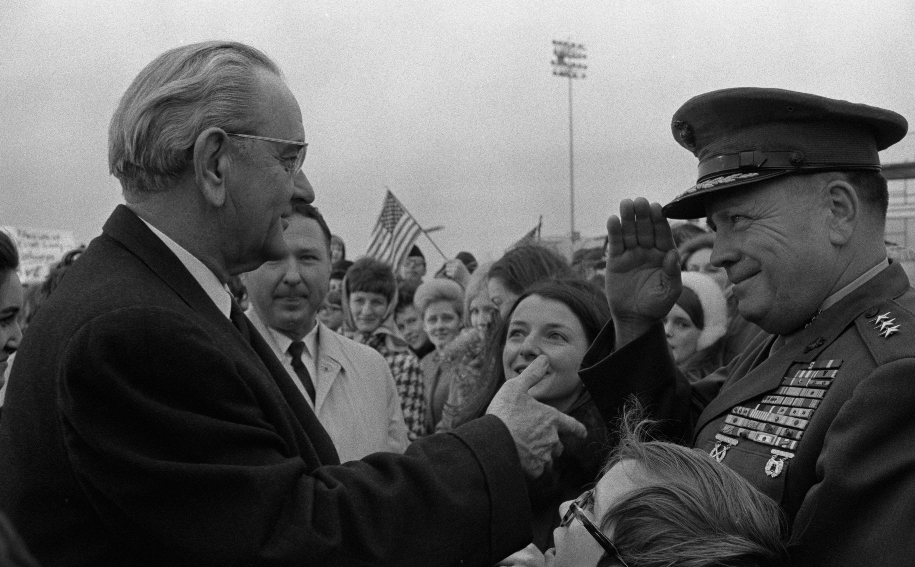 An officer salutes President Johnson as he shakes hands with supporters.